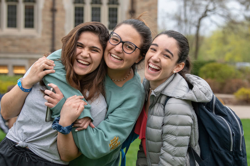Three young women happily embrace each other in front of a building, radiating joy and friendship.
