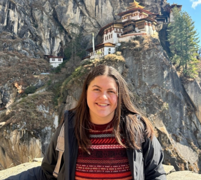 Senior Rose Quinlan posing in front of mountain with Bhutan-style building in background