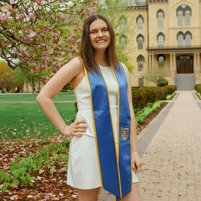 Megan Crawford '24 stands in front of the Main Building wearing graduation sash