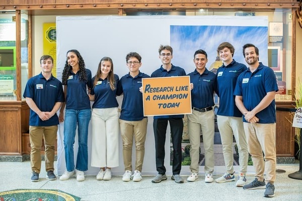 Levi Cherek ‘25 with group holding a "Research like a Champion Today" sign.