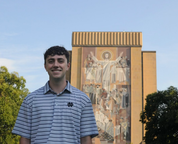 Johnny Blote '25 standing in front of Touchdown Jesus