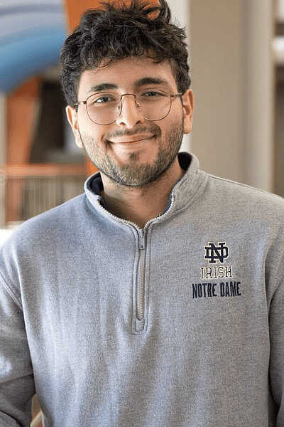 Mark Metryoos, a smiling young man in glasses and a grey quarter-zip sweatshirt with a navy ND Irish Notre Dame logo.